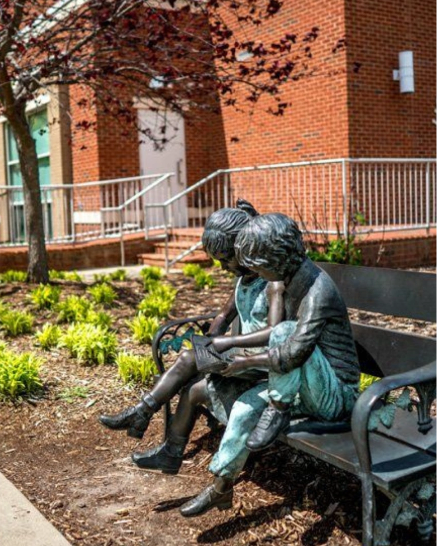 Bronze statue of two children sitting together on a bench near a brick building