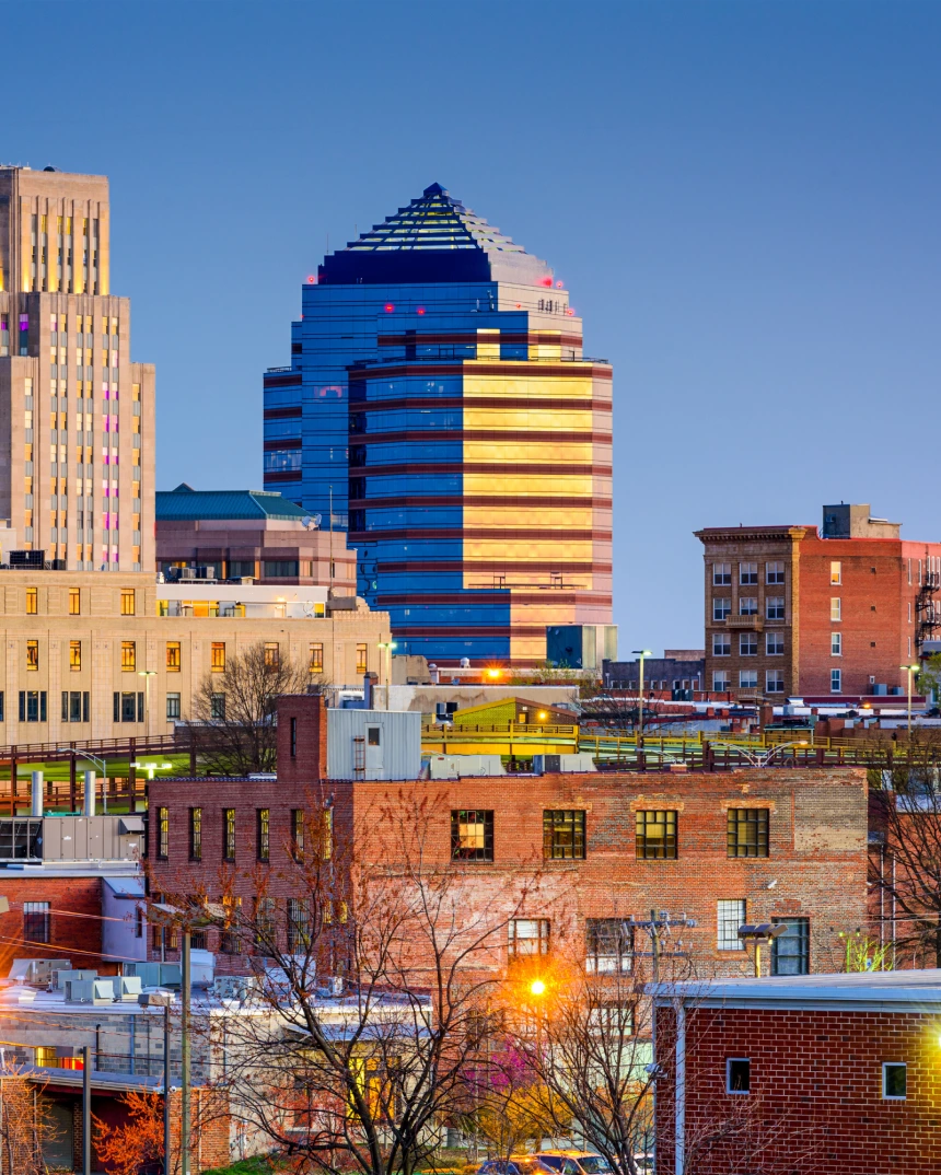 City skyline at dusk featuring a modern glass building with horizontal lights among older brick structures