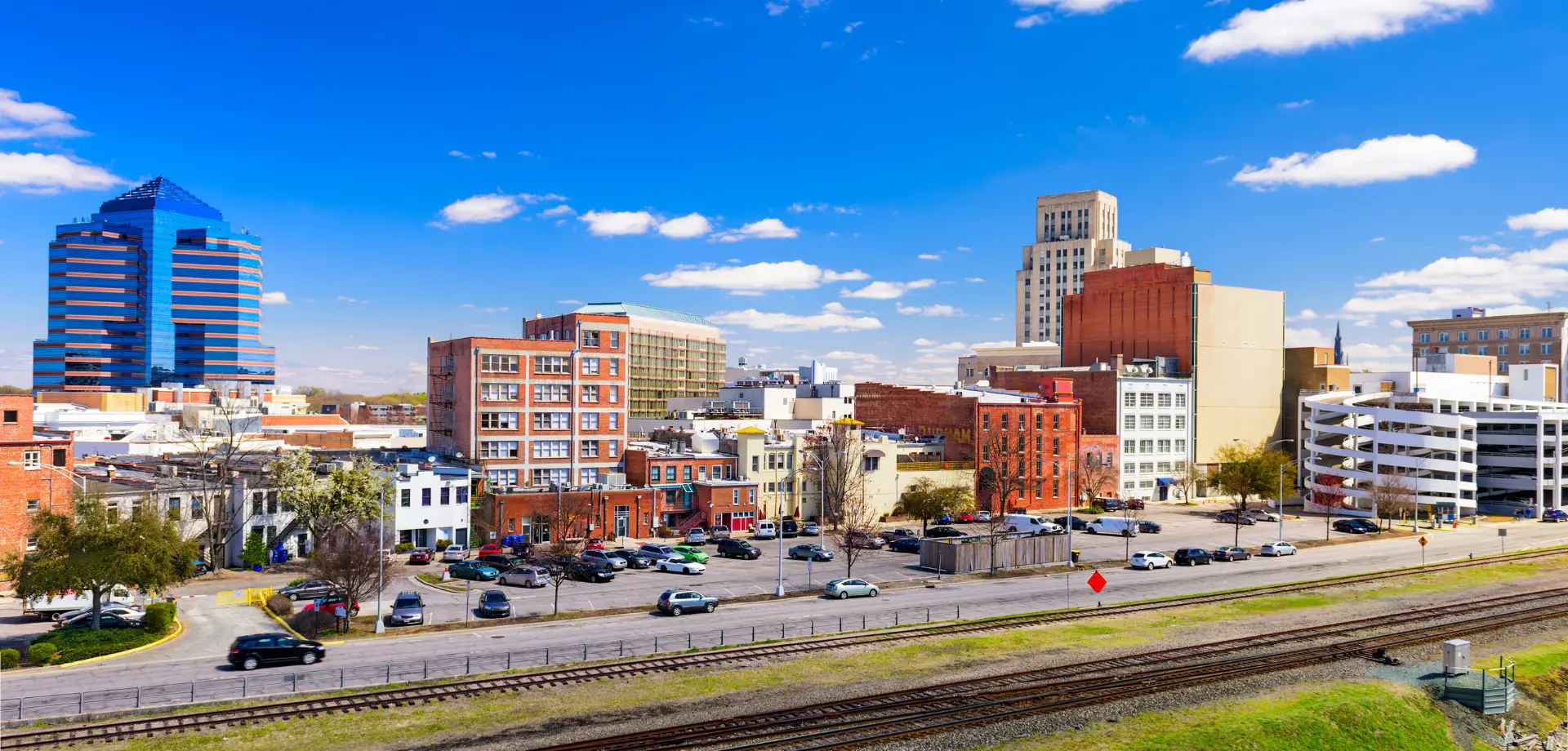 Cityscape with a mix of historic and modern buildings, seen from across train tracks under a bright blue sky