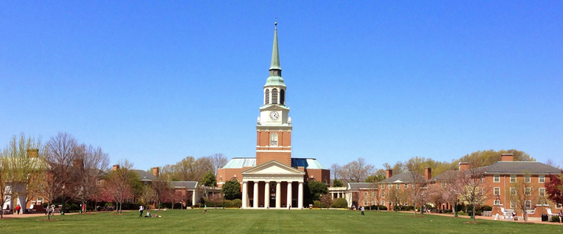 Large university building with a tall clock tower and steeple surrounded by a green lawn