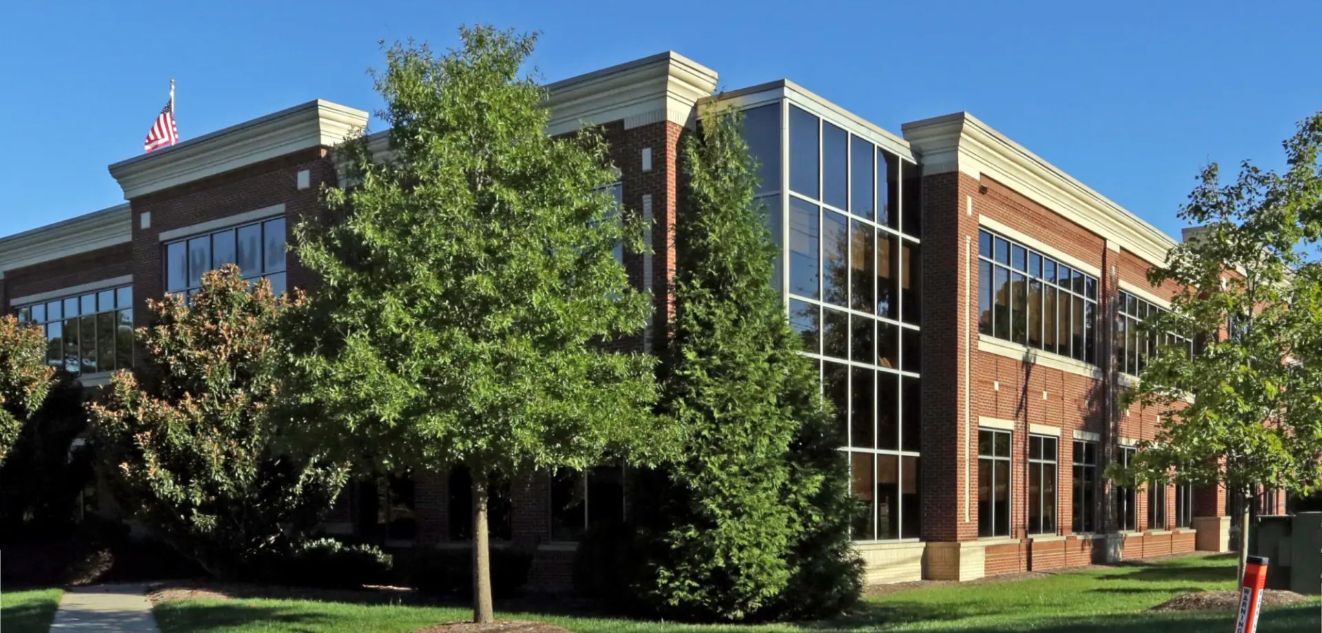 Modern brick office building with large glass windows surrounded by trees and greenery