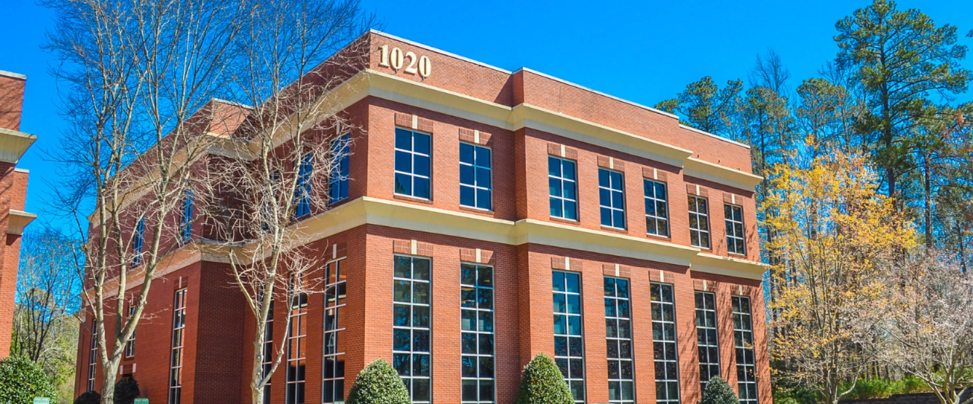 Red brick office building surrounded by trees under a clear blue