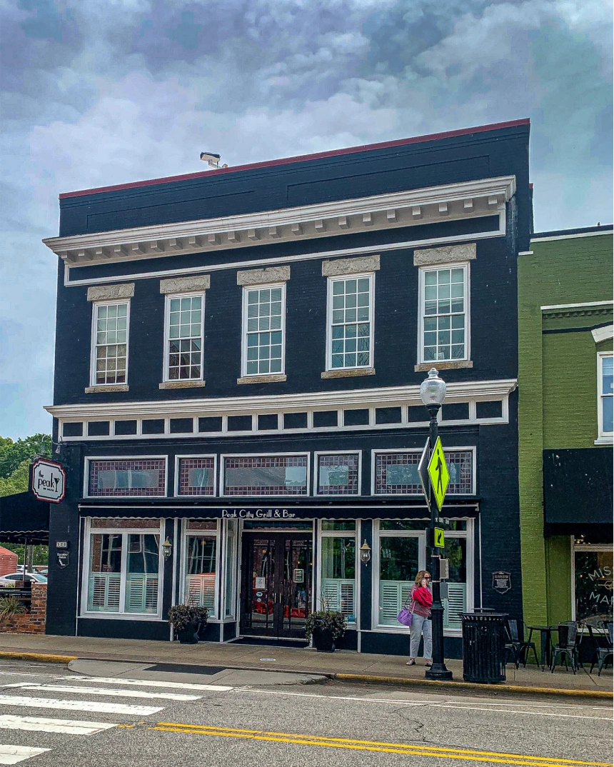 Two-story black-painted historic building with large windows and a person standing on the sidewalk